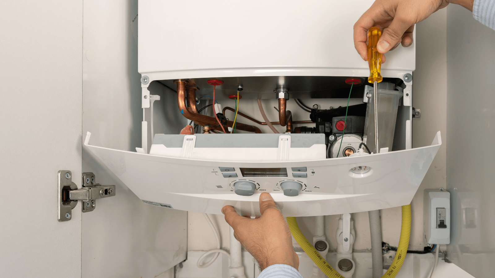 A person performing maintenance on a gas boiler, using a screwdriver to adjust components inside the unit.